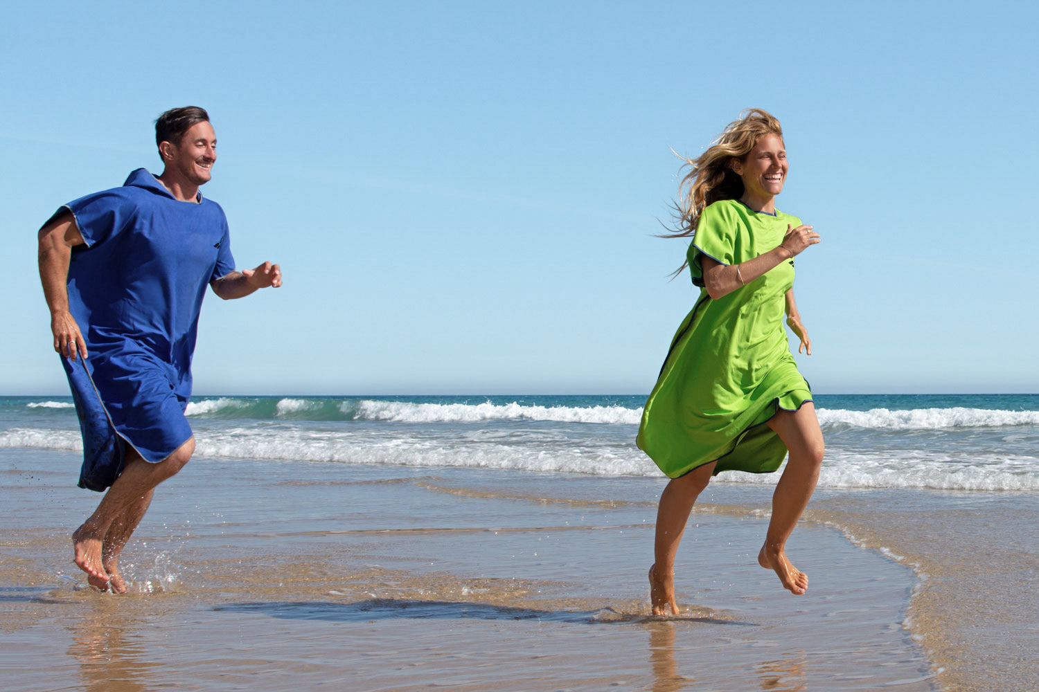 Frau und Mann laufen in Fit-Flip Poncho zum Surfen über den Strand